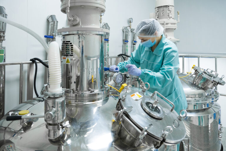 Pharmaceutical factory woman worker in protective clothing operating production line in sterile environment